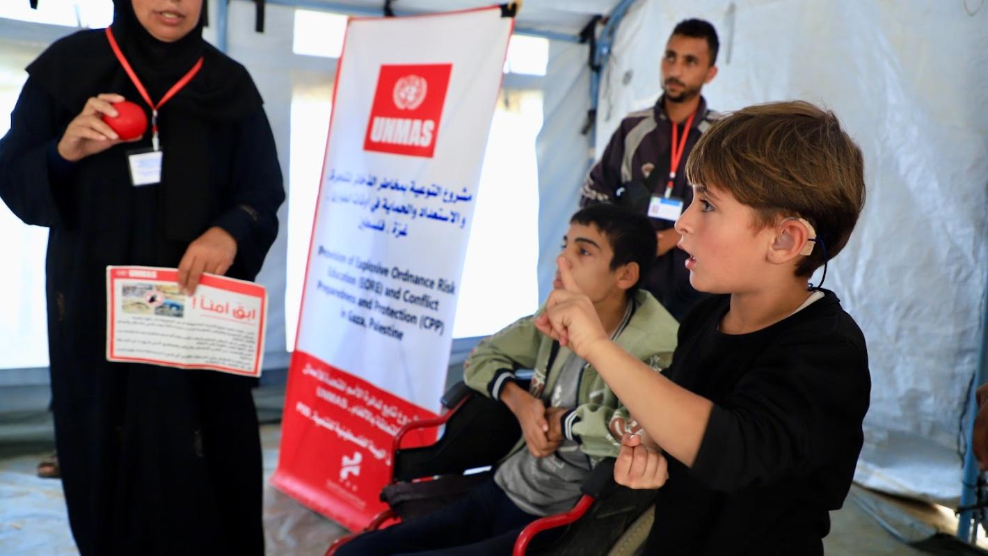 A woman is holding a red ball and a poster with two kids and a man beside her