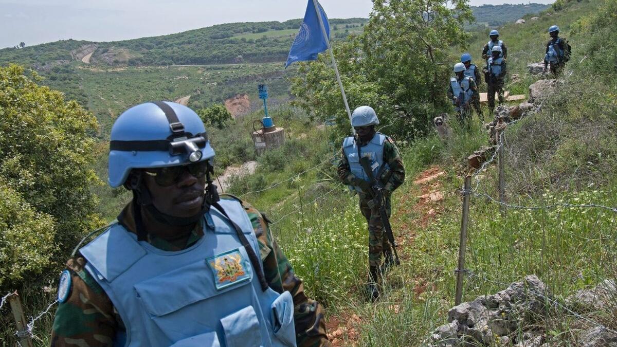 UN Peacekeepers trek through a field.